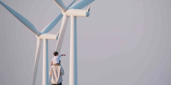 Child on adult's shoulders pointing at wind turbines on a clear day.