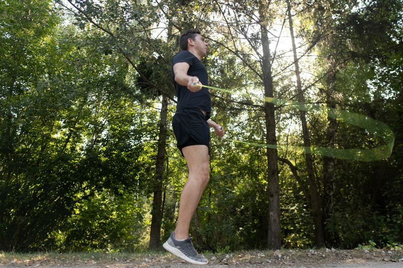 A man actively trains with a jump rope in a green park, boosting energy and strengthening his health.