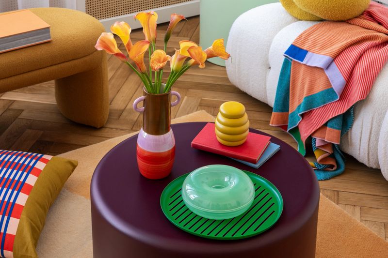 Stylish coffee table decor with orange calla lilies, colorful pillows, and bold design pieces. A chic blend of modern design and warm, playful accents for an inviting interior.