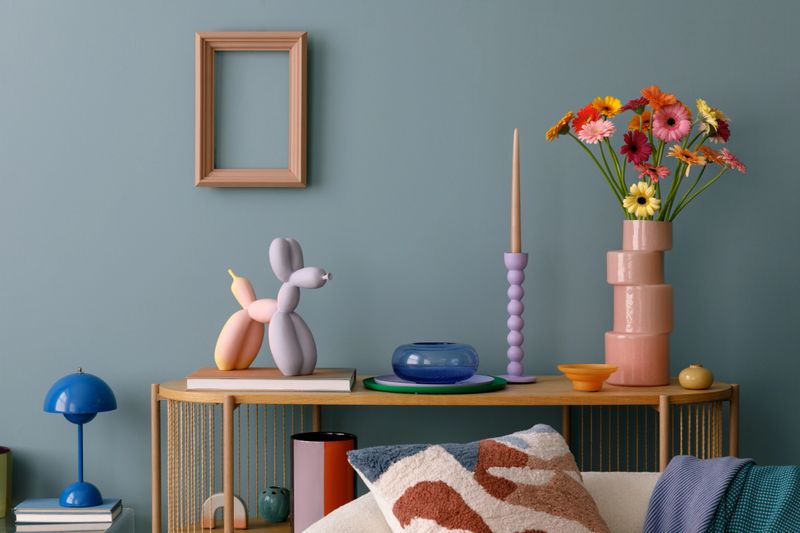 Modern decorative setup with vibrant flowers, a balloon dog sculpture, and colorful candle holders, set against a muted teal background.