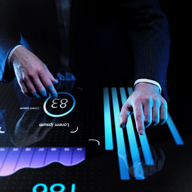 Businessman in dark suit interacting with futuristic touch screen displaying glowing blue bar charts and circular data interface against dark background. Concept of business, data, engineering. Ad