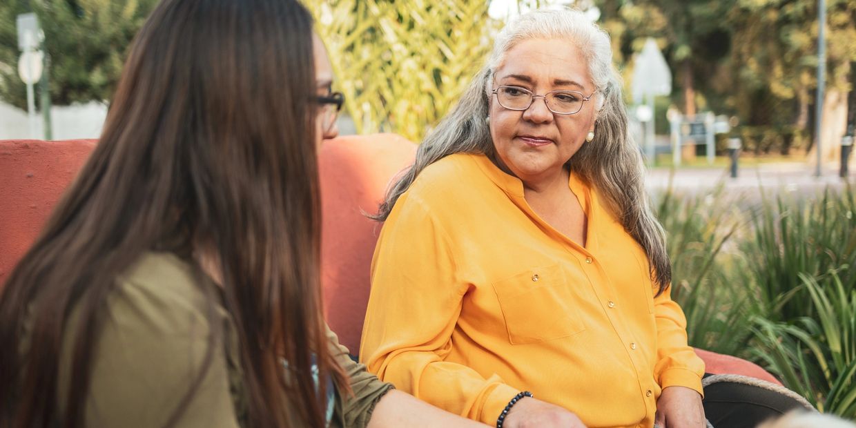 Two women engaged in a thoughtful conversation outdoors on a bench.
