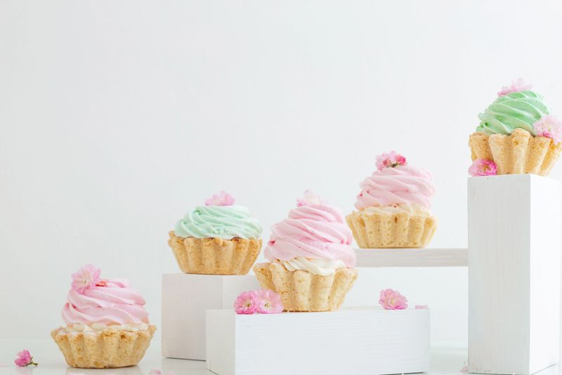 pink and green cupcakes with spring flowers  on wooden podiums on white  background