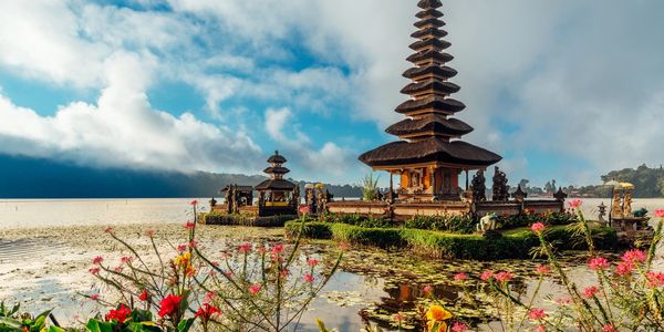 Traditional Balinese temple by the water with flowers in bloom.