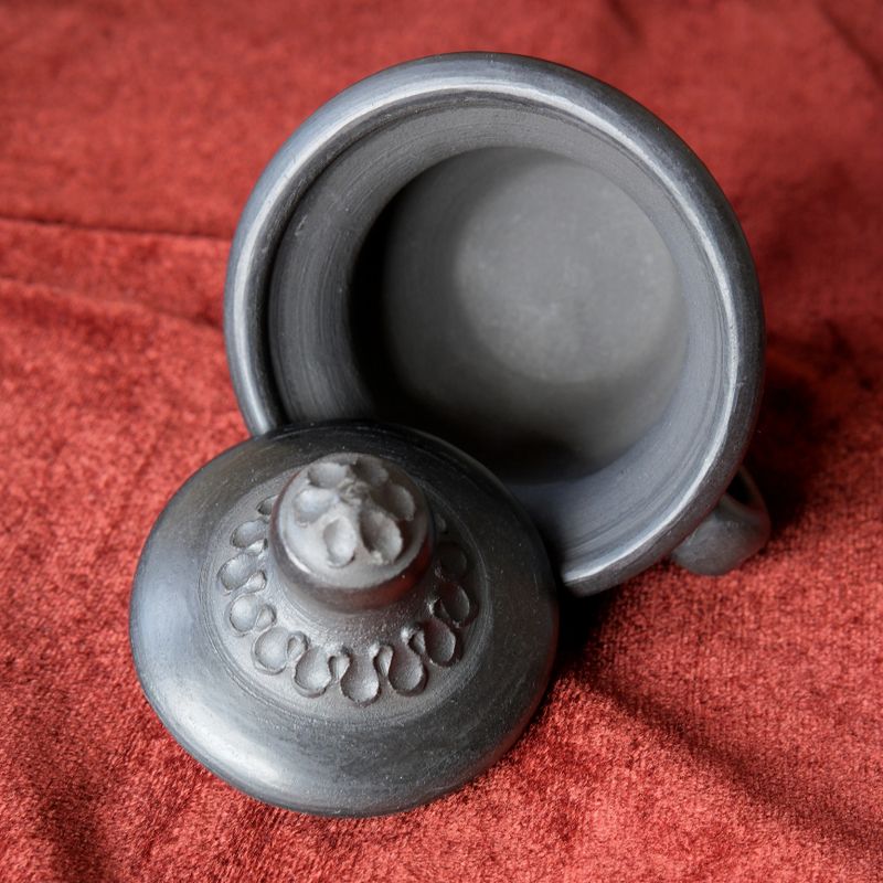 Intricate clay pot resting on rich fabric showcases unique craftsmanship.