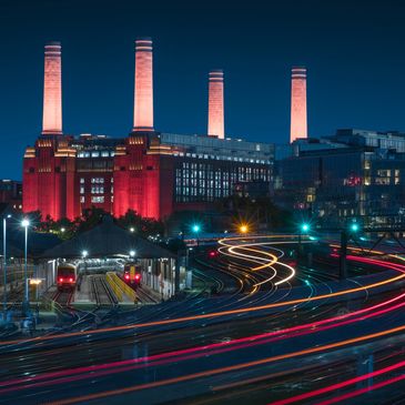 Night view of Battersea Power Station with light trails from trains.