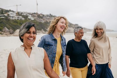 Four diverse women laughing and walking together on a beach.