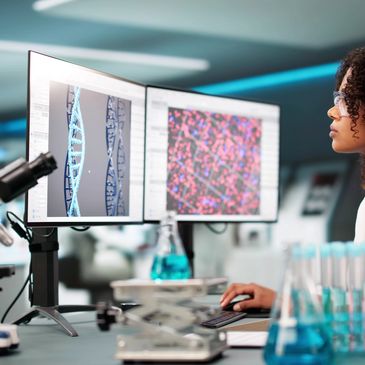 Scientist analyzing DNA and molecular data on dual monitors in a modern lab.