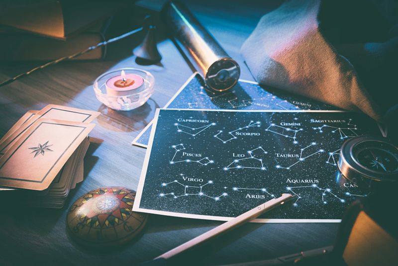 Esoteric astrological background detail with map with constellations, divination cards and retro objects on wooden table with magical atmosphere. Elevated view.