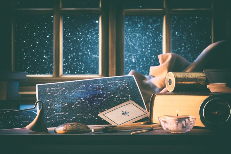 Astrological background of status and forecast with maps with constellations on wooden table with vintage objects and tools around and wooden window behind with starry sky in background. Front view.