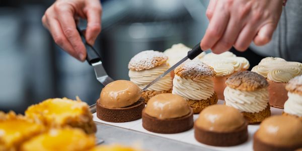 Hands carefully preparing elegant cream-filled pastries in a bakery.