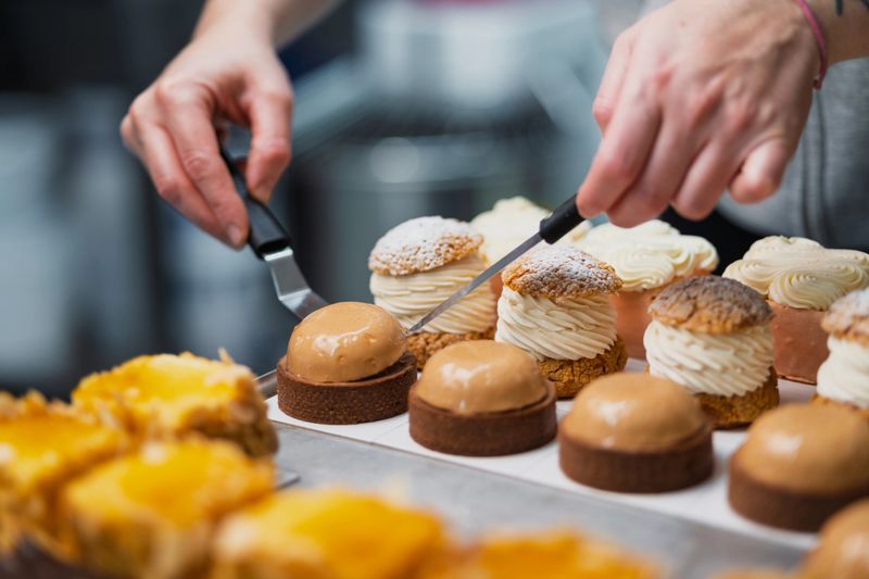 Close-up of a pastry chef's hands meticulously arranging delicious cream puffs and tarts on a tray, showcasing the artistry and precision of dessert making