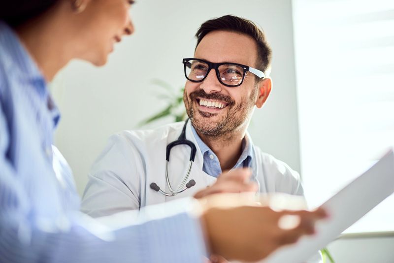 A cheerful male doctor engaged in a friendly discussion with a patient, conveying professionalism and care in a well-lit consultation room, emphasizing trust and communication in the medical field.