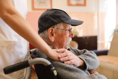 Caregiver supporting elderly man in wheelchair.
