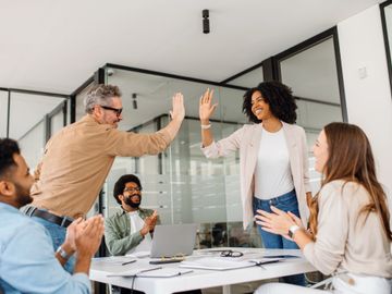 Colleagues celebrating a success with high-fives and applause in a modern office.