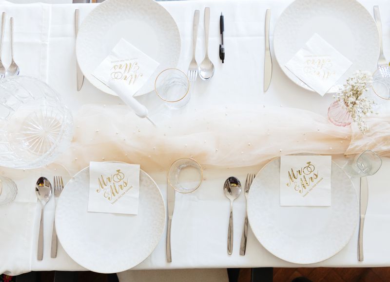 Beautiful view of wedding paper napkins with gold inscription: Mr. and Mrs. thank you for coming in empty plates on a festive table with veches and decorative flowers in vases, flat lay close-up. Concept party time, festive decoration.