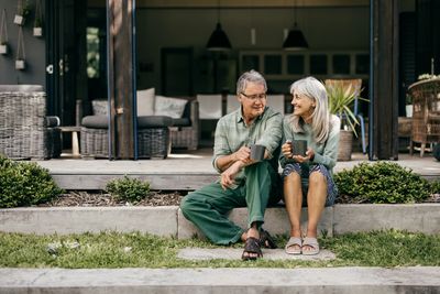 An elderly couple sitting on steps, enjoying coffee and smiling at each other.