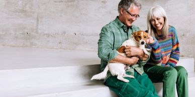 A happy elderly couple sitting and holding a small dog together.