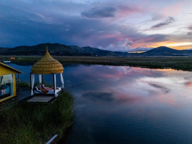 Golden sunset reflecting on calm lake beside mountain range. Peaceful lakeside scene at dusk with vibrant sky.