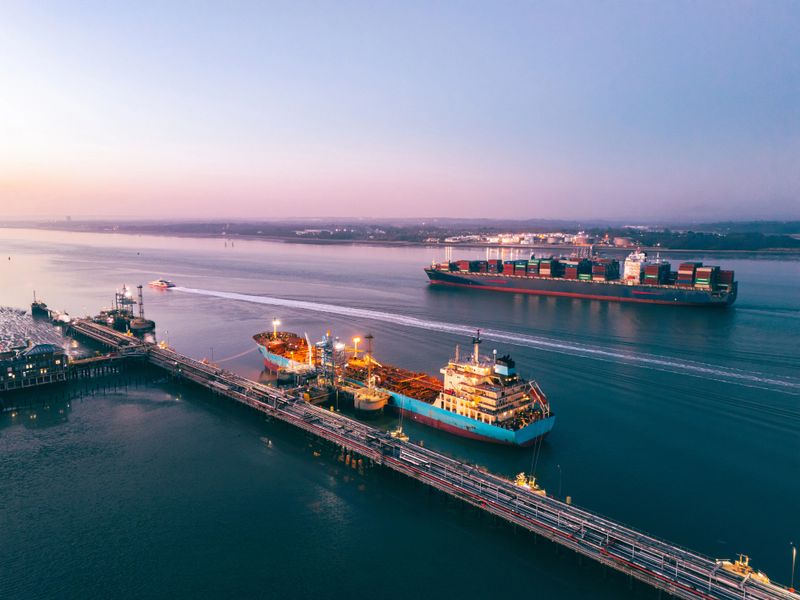 Aerial view of cargo ships navigating southampton water at dusk, with fawley oil refinery in the foreground