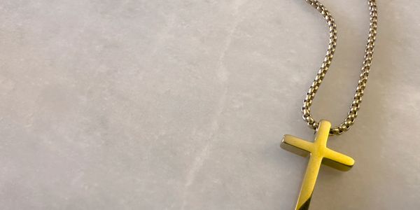 A gold cross pendant on a chain resting on a light surface.