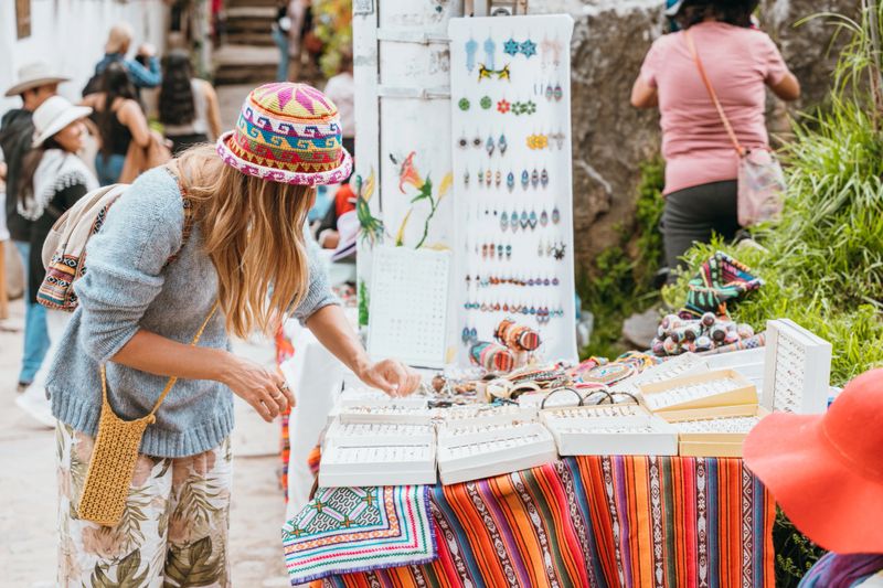 Young woman browsing handmade jewelry at vibrant outdoor market. Tourist exploring diverse artisan crafts in a bustling street market. Travel, shopping, and local culture.