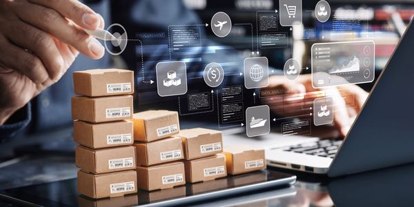 Stacked parcels on a digital tablet with virtual logistics icons and a laptop in the background.