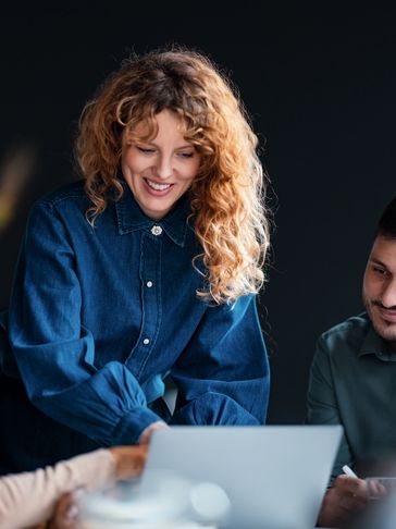 Three colleagues collaborating and smiling over a laptop in a modern office.