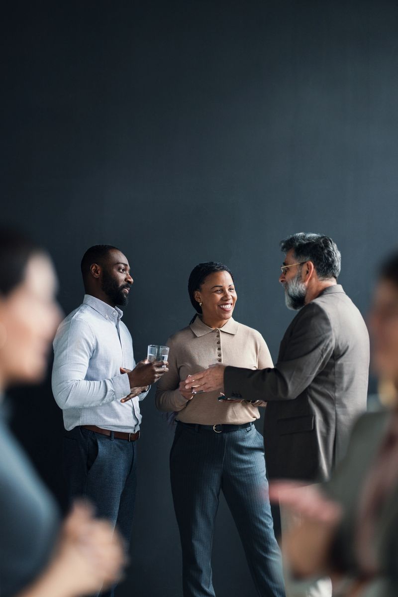 A group of business professionals engaging in conversation at a formal networking event. The setting encourages collaboration and relationship-building, representing a modern corporate atmosphere for meetings and discussions.