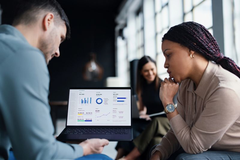 Office professionals collaborating on data analysis displayed on a laptop screen, seated in a well-lit workspace, discussing strategies and insights for their business goals and corporate objectives.