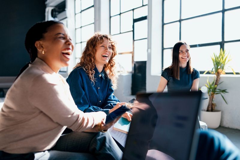 Colleagues sharing a moment of laughter and positivity during a casual meeting in a brightly lit, modern workspace, fostering team spirit and collaboration in a creative business environment.