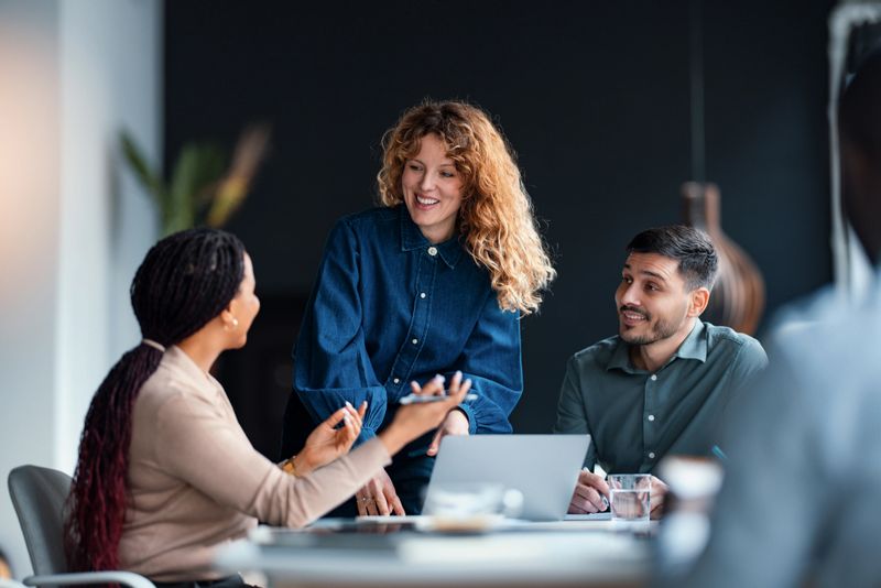 A group of diverse business professionals engaging in a collaborative meeting, showcasing teamwork, communication, and workplace interaction in a corporate setting with a modern office environment.