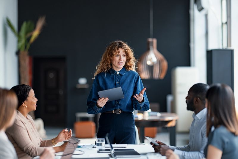 Confident businesswoman presents to a diverse team during a collaborative meeting in a stylish office environment, promoting teamwork and communication.