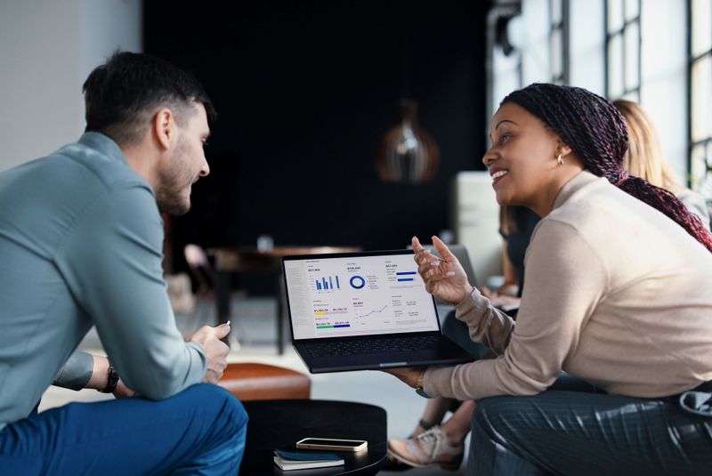 A professional business team collaborates, analyzing data presented on a laptop screen in a modern, bright office setting, fostering teamwork, productivity, and aligning on strategies for business success.