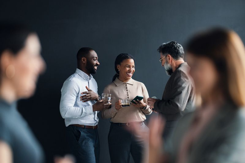 A diverse group of colleagues engaging in a casual conversation during a break, embracing networking and teamwork in a professional atmosphere. The exchange emphasizes camaraderie within business settings.