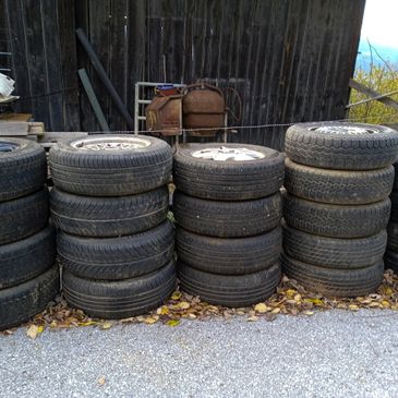 Stacks of used tires piled in front of a wooden shed outdoors.