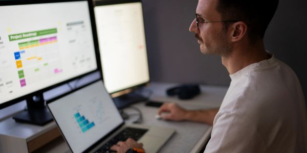 Man working on multiple screens with project planning charts visible.