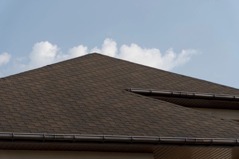 Modern tiled roof construction highlights quality workmanship on a residential house set against a bright blue sky with white clouds.