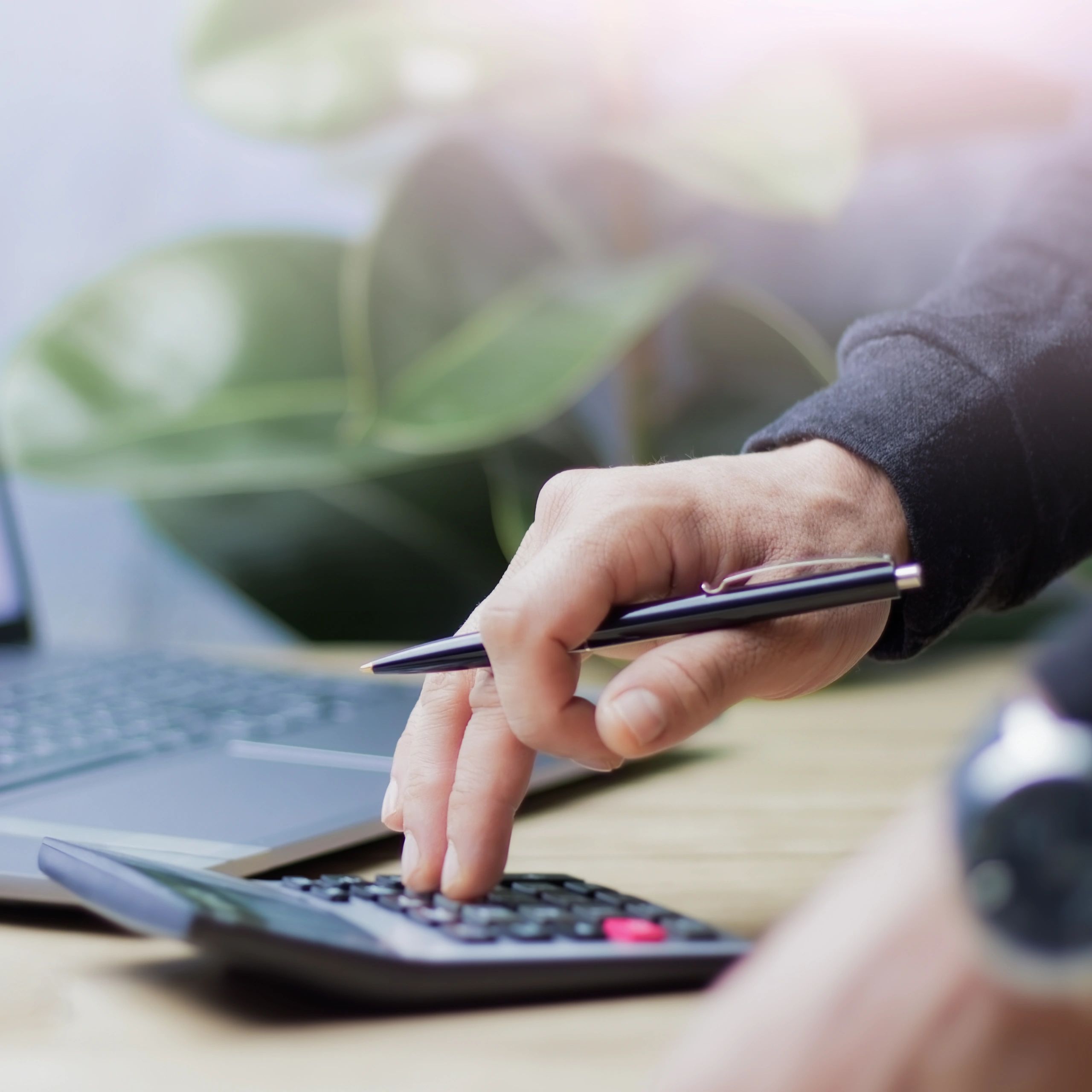 Person using calculator and laptop with pen in hand.