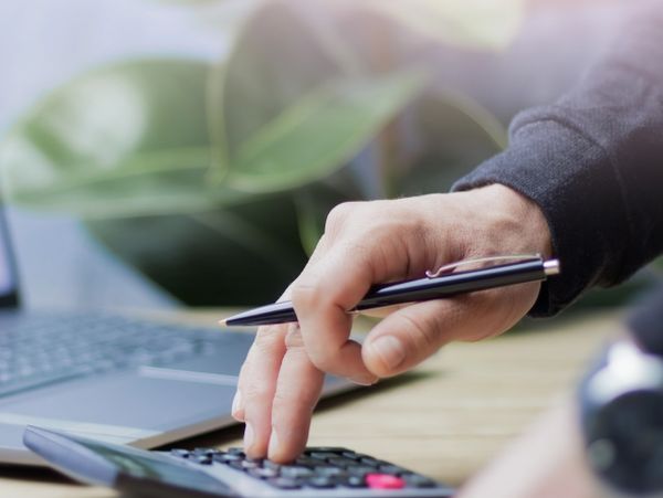 Person using a calculator with a pen in hand beside a laptop.