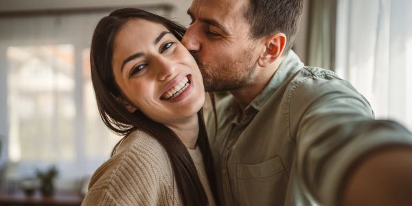 Couple taking a happy selfie, man kissing woman on cheek.