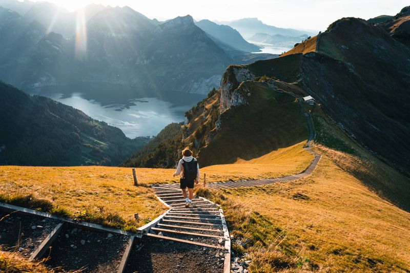 Young man hikes along pathway on mountain ridge above lake in autumn, distant scene, Fronalpstock, Schwyz  Canton, Swiss Alps