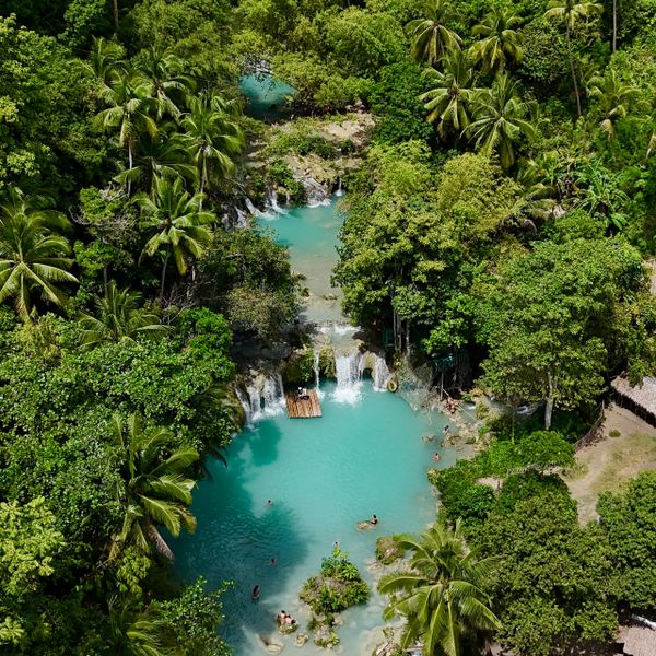 Tropical lagoon with waterfalls surrounded by dense forest and palm trees.