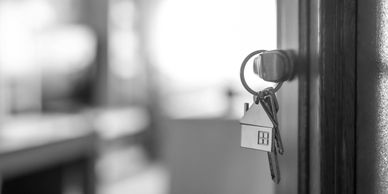 Keys with a house keychain hanging from a door lock in black and white.