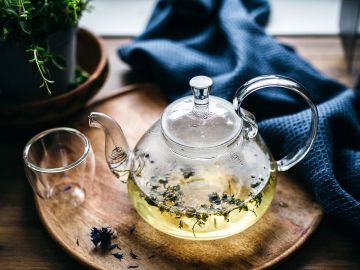 Glass teapot with herbal tea on a wooden tray.