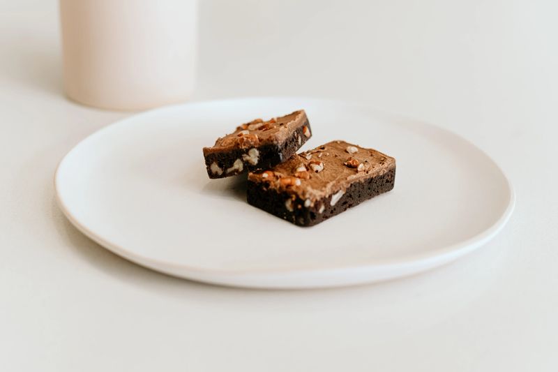 A cozy coffee break setup featuring a cup of coffee, chocolate brownies with nuts, and a neutral-toned vase on a minimalist kitchen counter.