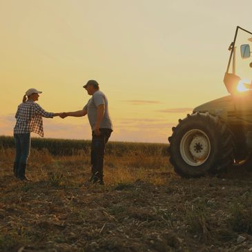 Farmers shaking hands near tractor at sunset.