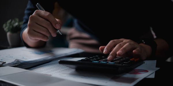 Person using a calculator and pen to analyze documents in low light.
