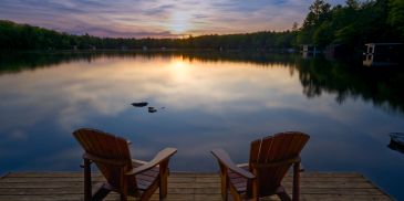 Two chairs on a dock overlooking a calm lake at sunset.