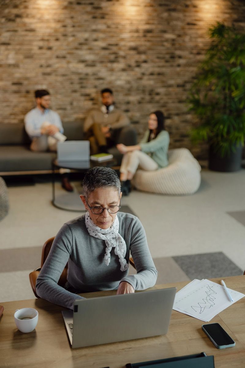 Focused professional working on a laptop at a modern office, with relaxed colleagues in the background, enhancing a collaborative and productive work atmosphere.